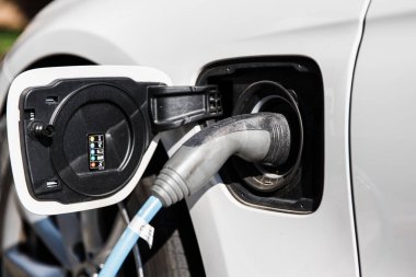 Elektrikli araba şarj etmek için güç kaynağı. Bir elektrikli otomobil soket takılı güç kaynağının kapatın. Beyaz otomobil parlak güneşli gün şarj ediliyor.