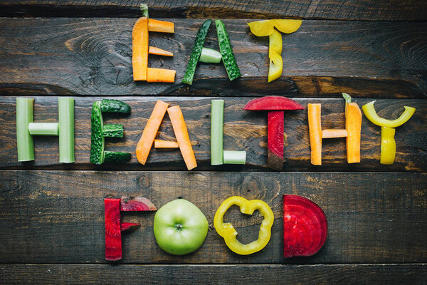Eat healthy food fresh vegetables flat lay lettering on dark wooden table top view. Nutrition organic meal ingredients concept. Nice cooking postcard, poster, banner.
