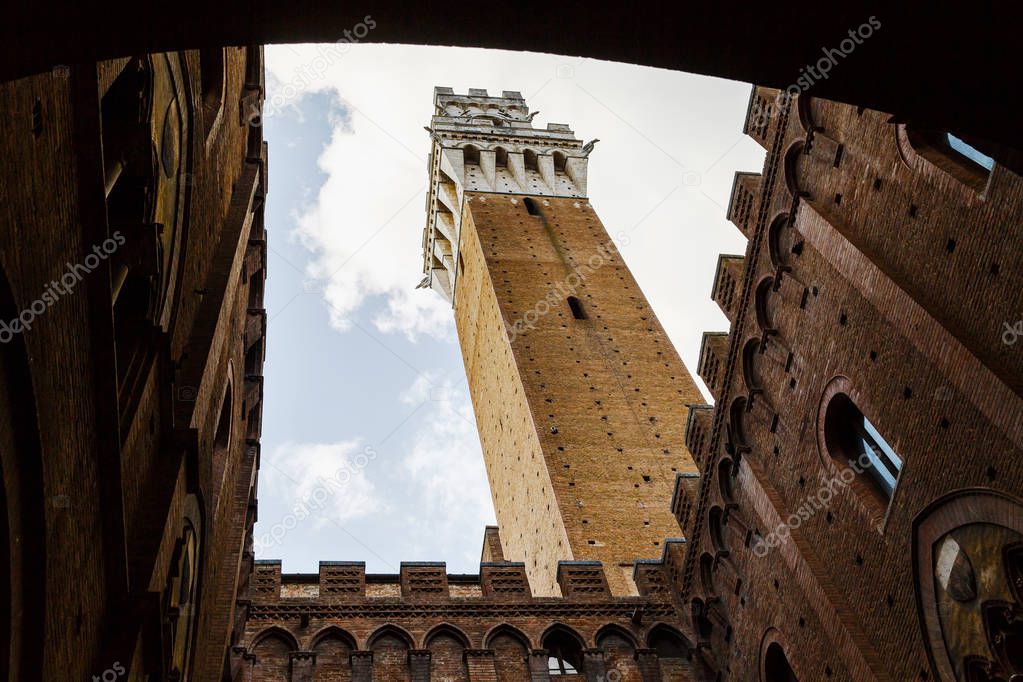 Picturesque bottom view of Torre del Mangia (Mangia tower) from inside of Palazzo Publico inner courtyard in Siena, Tuscany, Italy. Scenic travel destination postcard.