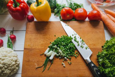 Hala salata pişiriyorum. Bıçak ve taze taze soğan dilimleme tahtası üst görüşünde. Sebzeler sınır çerçevesi.