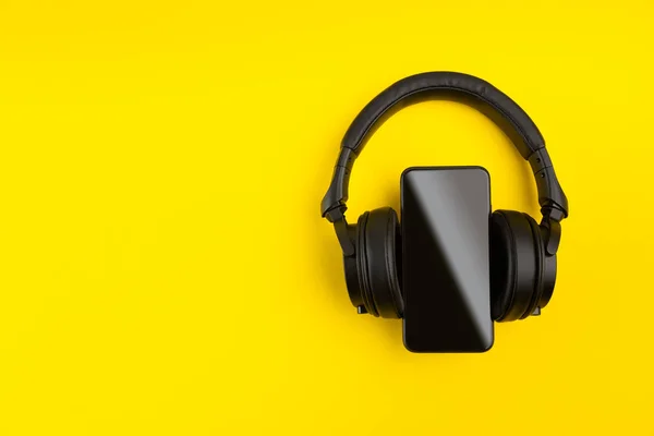 黑色无线耳机和智能手机在明亮的黄色彩色背景 带有复制空间的移动音乐应用创意最小概念 — 图库照片