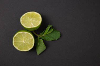 Yarısı kesilmiş kireç ve nane yaprakları soyut siyah arkaplanda fotokopi alanı ile. Koyu meyve kavramı.