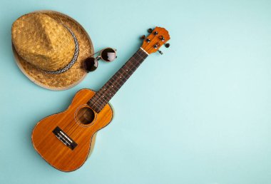 Ukulele ve saman şapkalı yaz tatili konsepti soyut pastel turkuaz arka planda fotokopi alanı ile. Yaratıcı düz yatak.