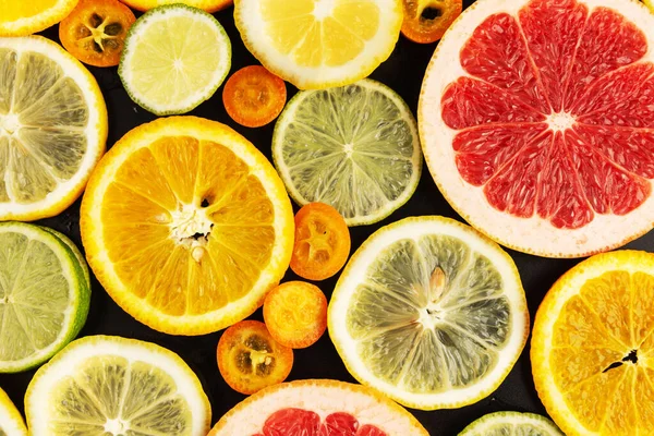 Assorted citrus fruits slices pattern on abstract black background. Juicy summer diet concept.