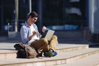 Mutlu gülümseyen yakışıklı başarılı erkek girişimci zaferi kutluyor ve projeyi bitiriyor. Mesaj için yer var. Şehirde defteri olan bir adam var..