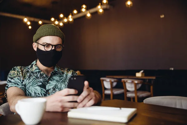 Μοντέρνο Έξυπνο Hipster Αρσενικό Φορώντας Χειροποίητη Μάσκα Προσώπου Χρησιμοποιώντας Smartphone — Φωτογραφία Αρχείου