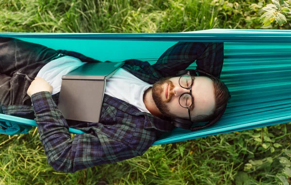 Der Bärtige Hipster Mann Liegt Mit Buch Der Hängematte Und lizenzfreie Stockbilder