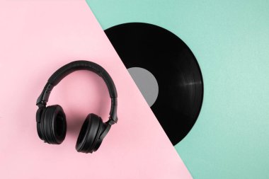 Soyut pastel renk bloğu arkaplanındaki vinil plak diski ve kulaklıkların üst görüntüsü. Müzik konsepti.