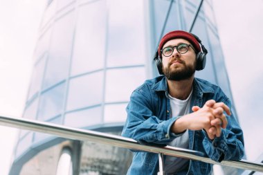 Kot gömlek giymiş düşünceli genç sakallı adam şehirde kulaklıkla mistik şeylerden hoşlanıyor. Uzaklara bakıyorum..