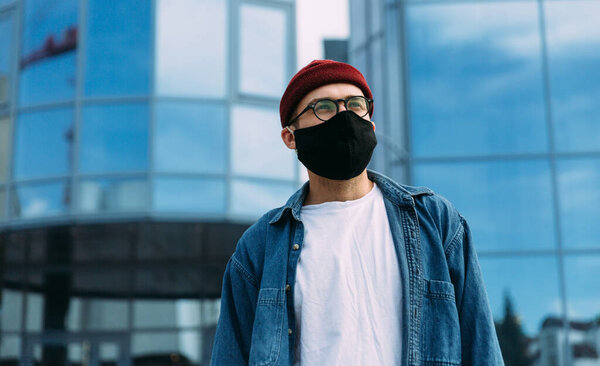 Stylish male hipster in business district wearing black virus mask looking away. Copy space. Virus concept.