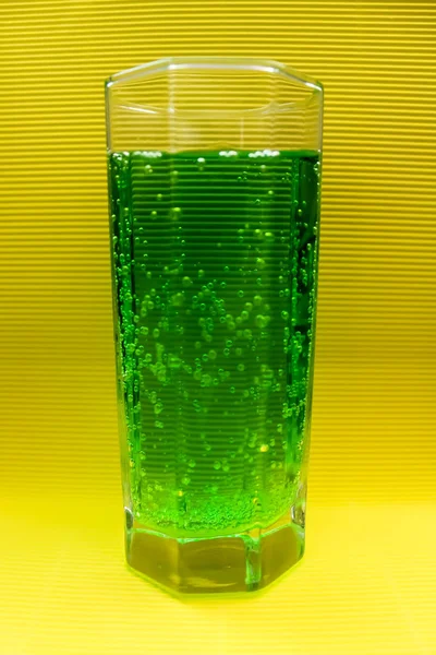 Glass beaker with green carbonated drink on a yellow background