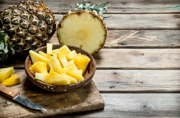 Sliced pineapple in a bowl on a cutting Board with a knife and a whole pineapple.