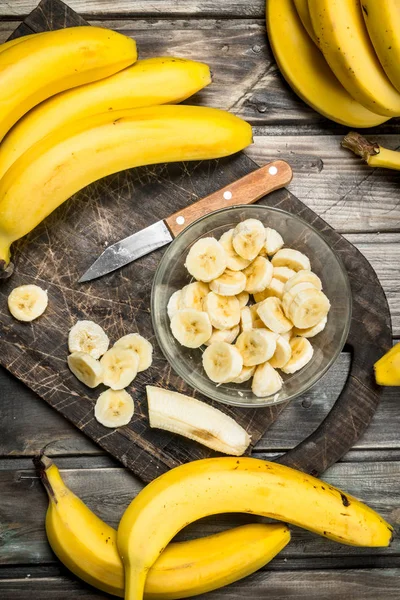 Bananas and banana slices in a plate on a black chopping Board with a knife.