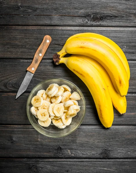 Fragrant bananas and banana slices in a glass bowl with a knife.