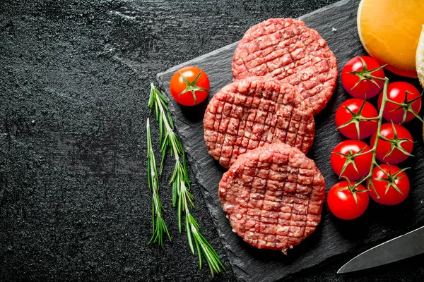 Raw burgers with cherry tomatoes, bread and rosemary.