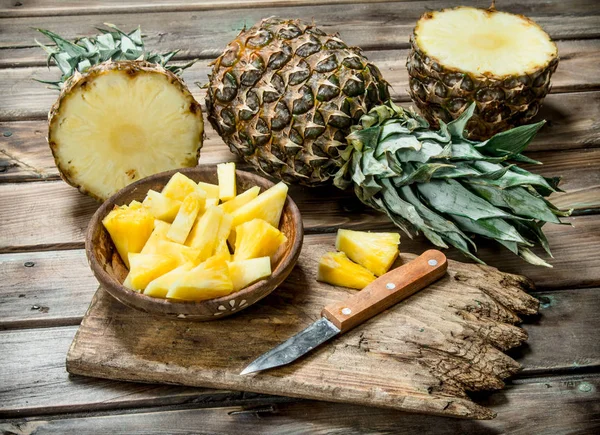 Sliced pineapple in a bowl on a cutting Board with a knife and a whole pineapple.