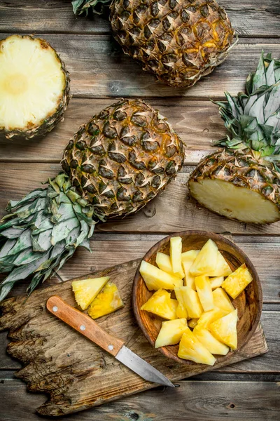 Sliced pineapple in a bowl on a cutting Board with a knife and a whole pineapple.