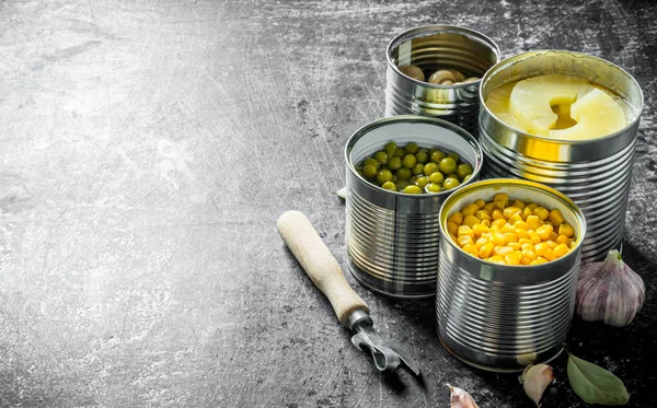 Canned pineapples, green peas, corn and mushrooms in open cans.