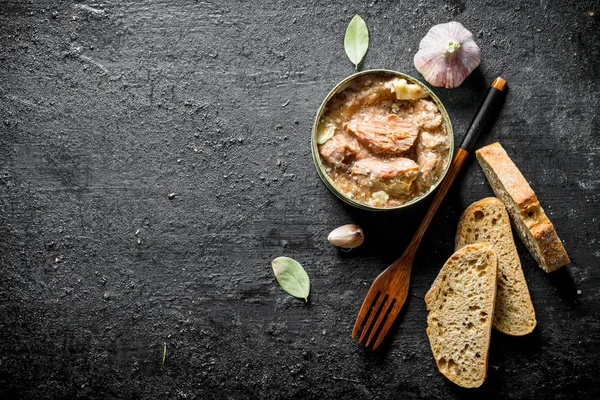 Canned meat in a tin with a fork and slices of bread.