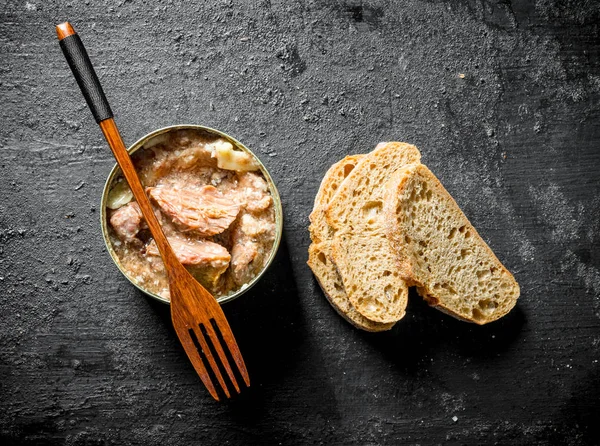 Canned meat in a tin with a fork and slices of bread.