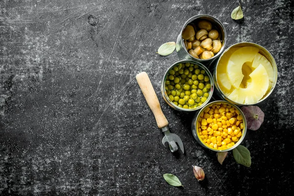 Canned pineapples, green peas, corn and mushrooms in open cans.