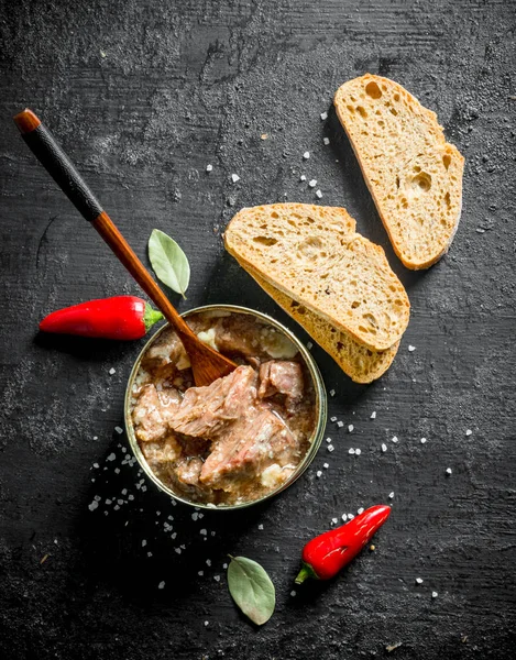 Open jar with canned meat with hot red pepper and bread.