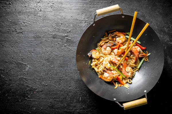 Chinese Udon noodles in a wok pan with chopsticks.