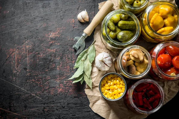 Pickled vegetables in jars on the paper with the Bay leaves and the cloves of garlic.