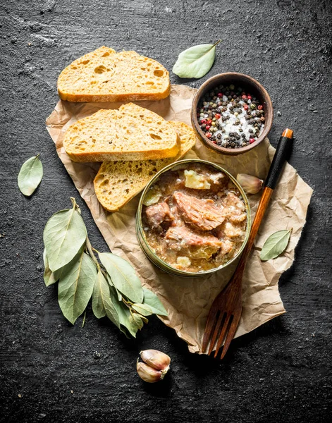 Canned meat in a tin on paper with slices of bread.