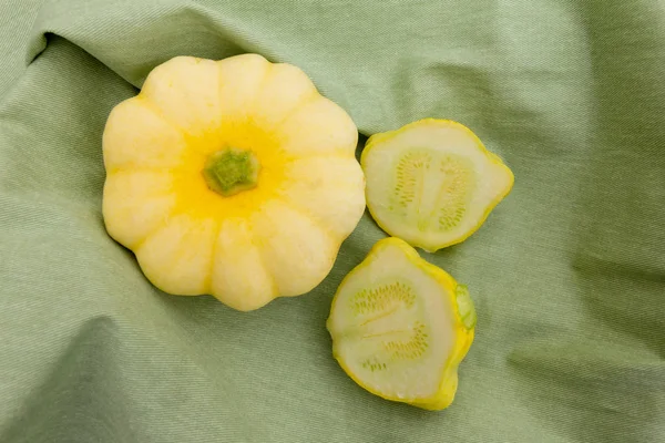 Whole and sliced patty pan squash on a green fabric background