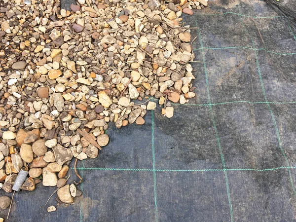 Weed control fabric-  half covered with stones and pebbles.