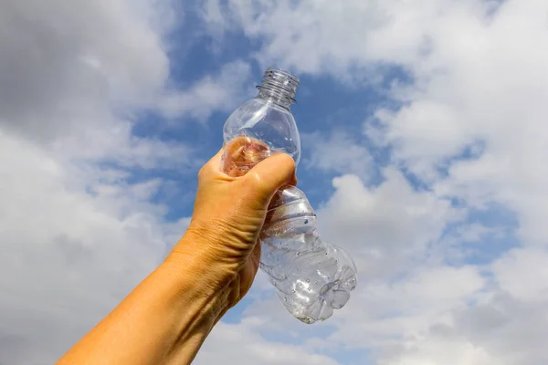 Holding a crumpled empty plastic drinks bottle against a sky background