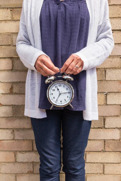 Middle aged woman holding a clock - time passing or biological clock concept