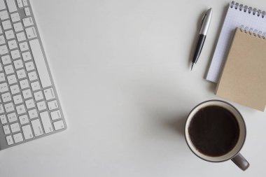 Beyaz ahşap masa klavye, kulaklık, kalem, Not defteri ve bir fincan kahve. Kopya alanı ile çalışma alanı üstten görünüm.