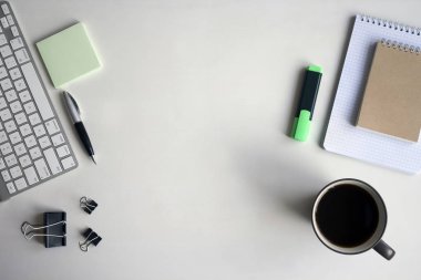 Beyaz ahşap masa klavye, yeşil marker, kalem, defter, belge klipleri ve bir fincan kahve. Kopya alanı ile çalışma alanı üstten görünüm.