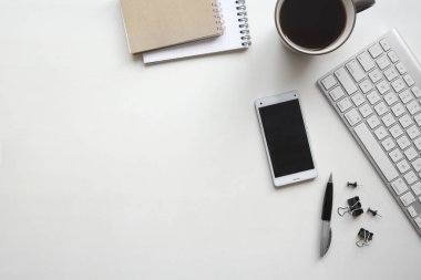Beyaz ahşap masa klavye, smartphone, kalem, defter, belge klipleri ve bir fincan kahve. Kopya alanı ile çalışma alanı üstten görünüm.