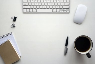 Klavye, fare, kalem, defter, belge klipleri ve bir fincan kahve ile beyaz ahşap masa. Kopya alanı ile çalışma alanı üstten görünüm.