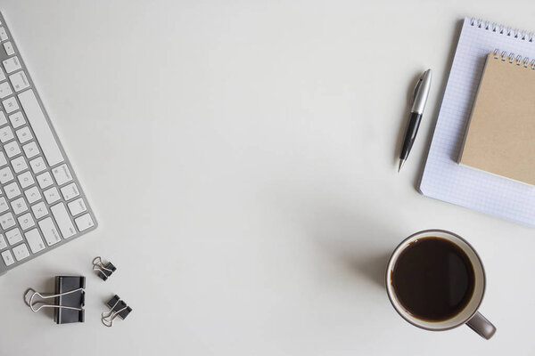 White wooden table with keyboard, pen, notebook, document clips and a cup of coffee. Workspace top view with copy space.