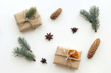 El işi kağıdında noel hediyesi olan kompozisyon, kurutulmuş portakal ve mandalin, anason yıldızları, tarçın, kozalak, beyaz arka planda köknar dalları. Düz yatış, üst görünüm