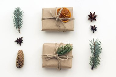 El işi kağıdında noel hediyesi olan kompozisyon, kurutulmuş portakal ve mandalin, anason yıldızları, tarçın, kozalak, beyaz arka planda köknar dalları. Düz yatış, üst görünüm