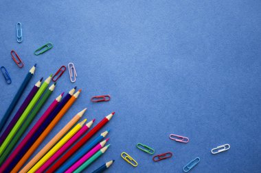 Okul malzemeleri üst görünüm - renkli kalemler, klipler - kopya alanı ile mavi arka plan üzerinde