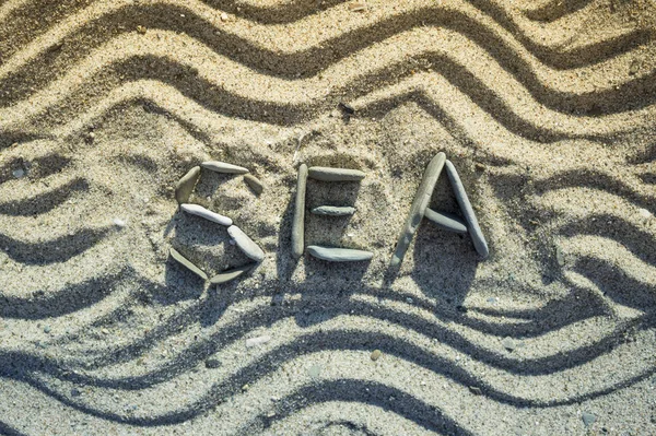 在沙滩上用鹅卵石和波浪形状制成的字海 — 图库照片