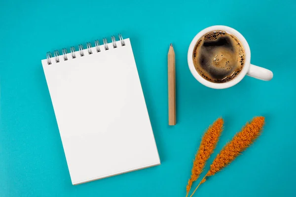 Notebook, coffee, pencil, orange spikelets on turquoise background. Workspace concept. Top view, copy space, mockup, flat lay