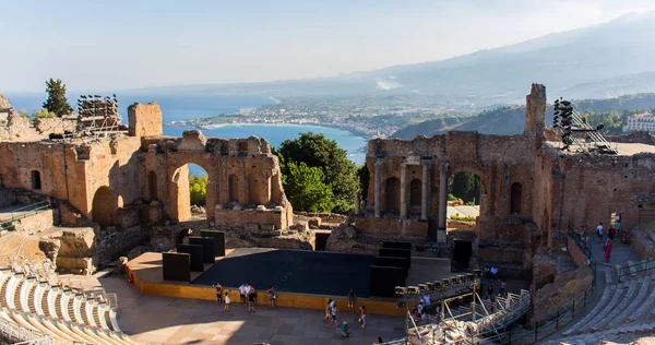 Ruins of the antique greek theater of Taormina in Sicily, with the smoking Etna in the background. Sunny summer day in Giardini-Naxos bay on the Ionian see. - Image