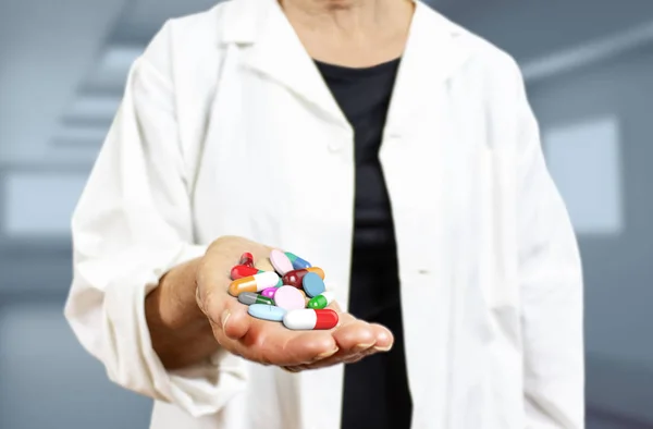 Old woman doctor holding pills, capsules, drugs and medics on a blurred blue hospital background 3d rendering. Medicine, health care, overmedication and disease healing concept.