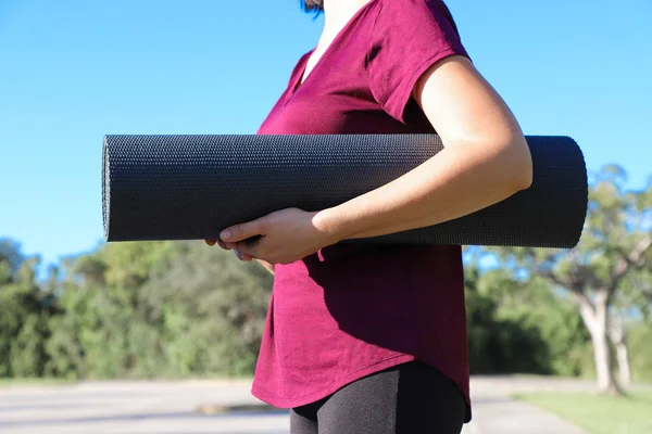 Close-up woman holding roll fitness or gray yoga mat after working out in the park. Healthy life concept