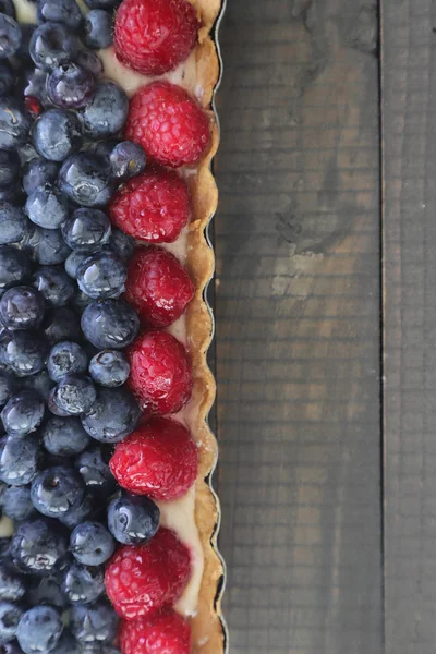 Appetizing close up of a berry tart consisting of blueberries and raspberries, On wooden background. Homemade tart with berry