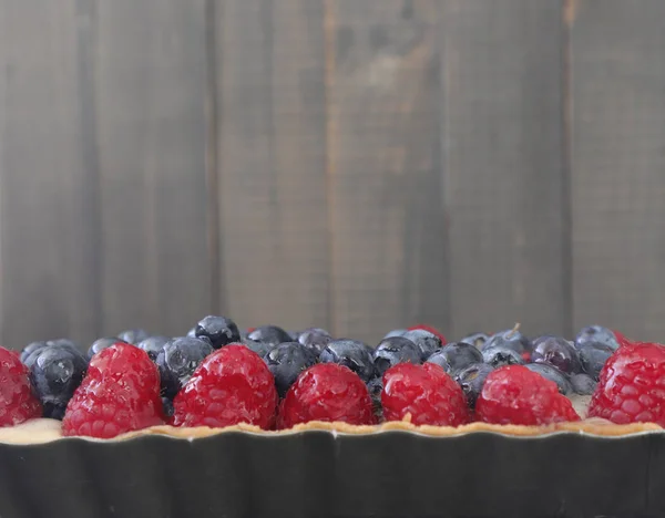 Appetizing close up of a berry tart consisting of blueberries and raspberries, On wooden background. Homemade tart with berry