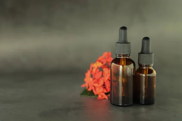 Koyu kozmetik şişeler, pembe çiçekli dal. gri bir arka plan üzerinde. Kopya alanı. Dostu doğal kozmetik konsepti. Minimalizm. Güzellik blogger, spa salonu, terapy salon.