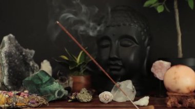 Masanın üzerinde tütsü çubuğu ve mumla Buda kafası heykeli.